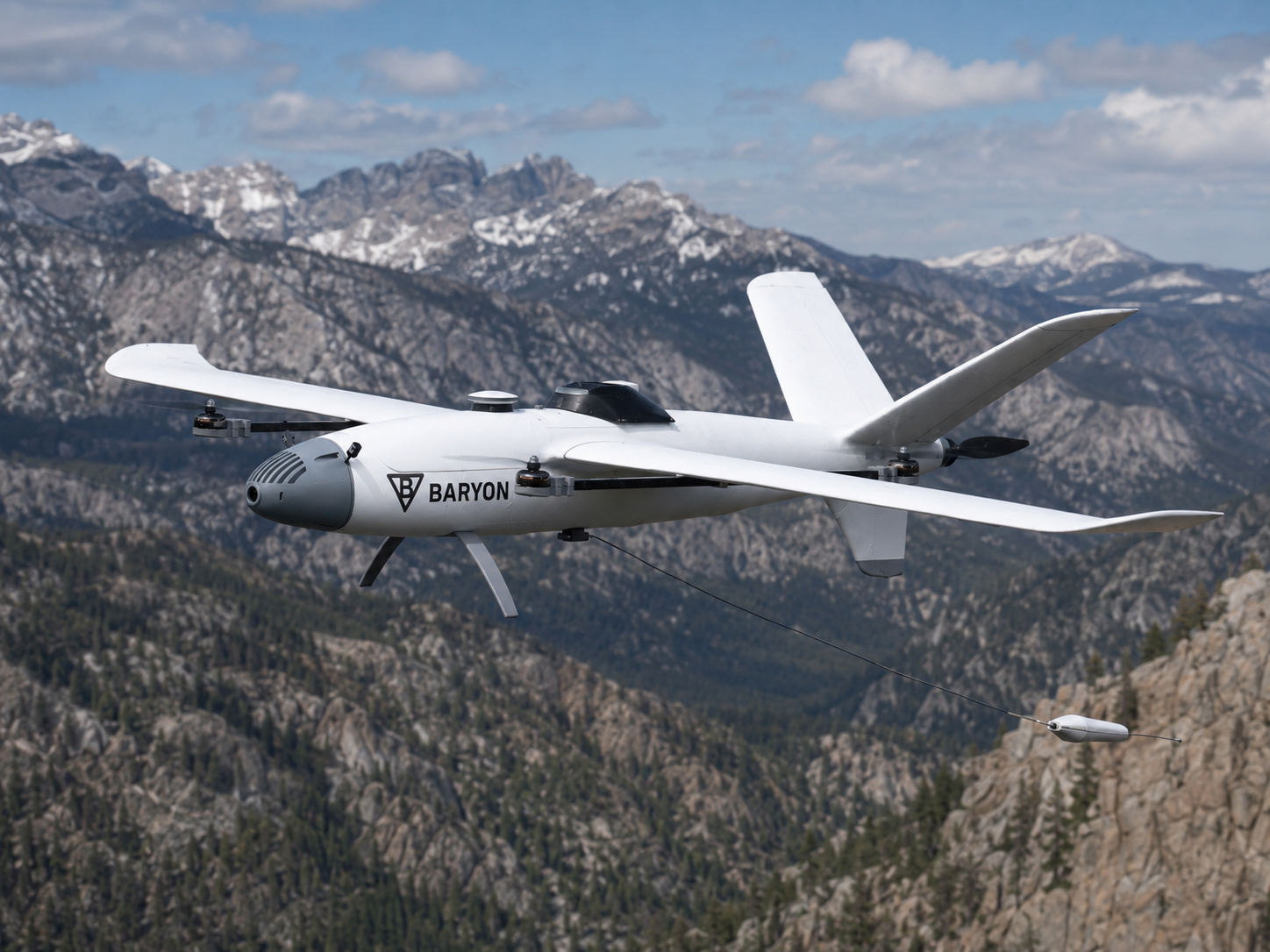 Baryon Aerial Scout VTOL aircraft in flight over mountains with towed magnetometer deployed